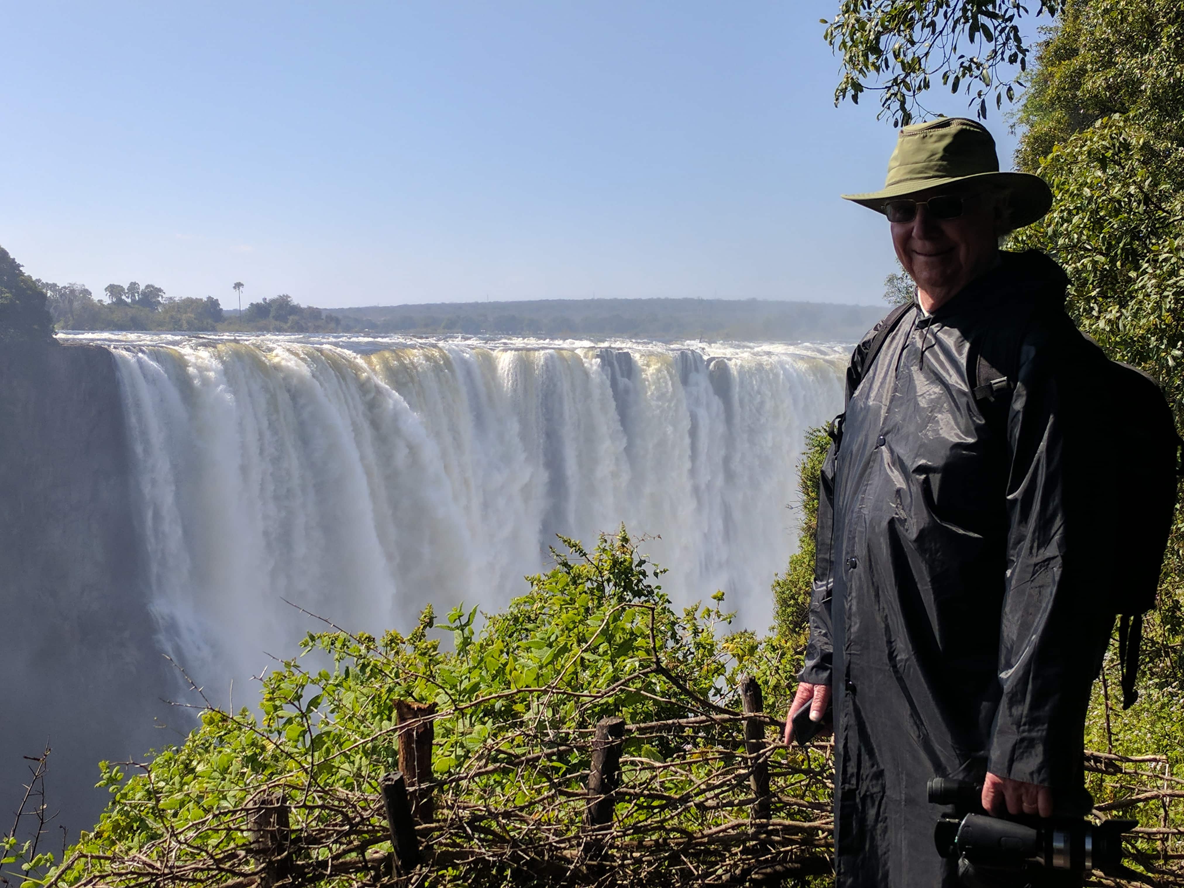 Person by a majestic waterfall in lush surroundings.